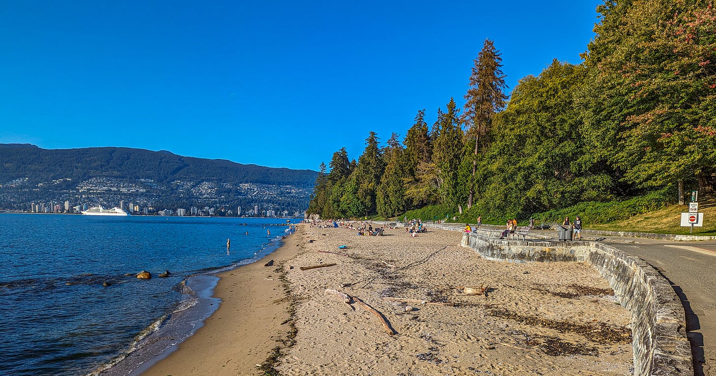 English Bay with Stanley Park in the back filled with trees. 