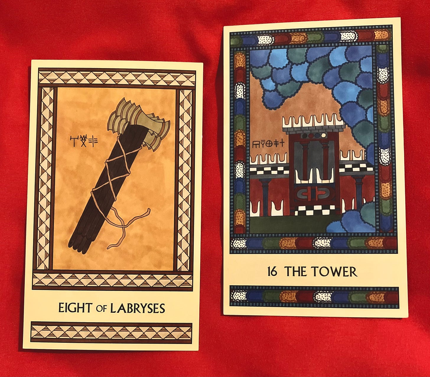 Two Minoan Tarot cards side by side on a bright red fabric surface. The Eight of Labryses is in shades of gold, cream, and tan. It shows a stack of eight labryses with their handles all together, apparently bound by rope. But close inspection shows that the rope is not actually knotted or tied; the ends hang loose. The Tower shows a Minoan temple, its roof topped by multiple pairs of sacred horns. It is being inundated by a tidal wave that crashes over it.