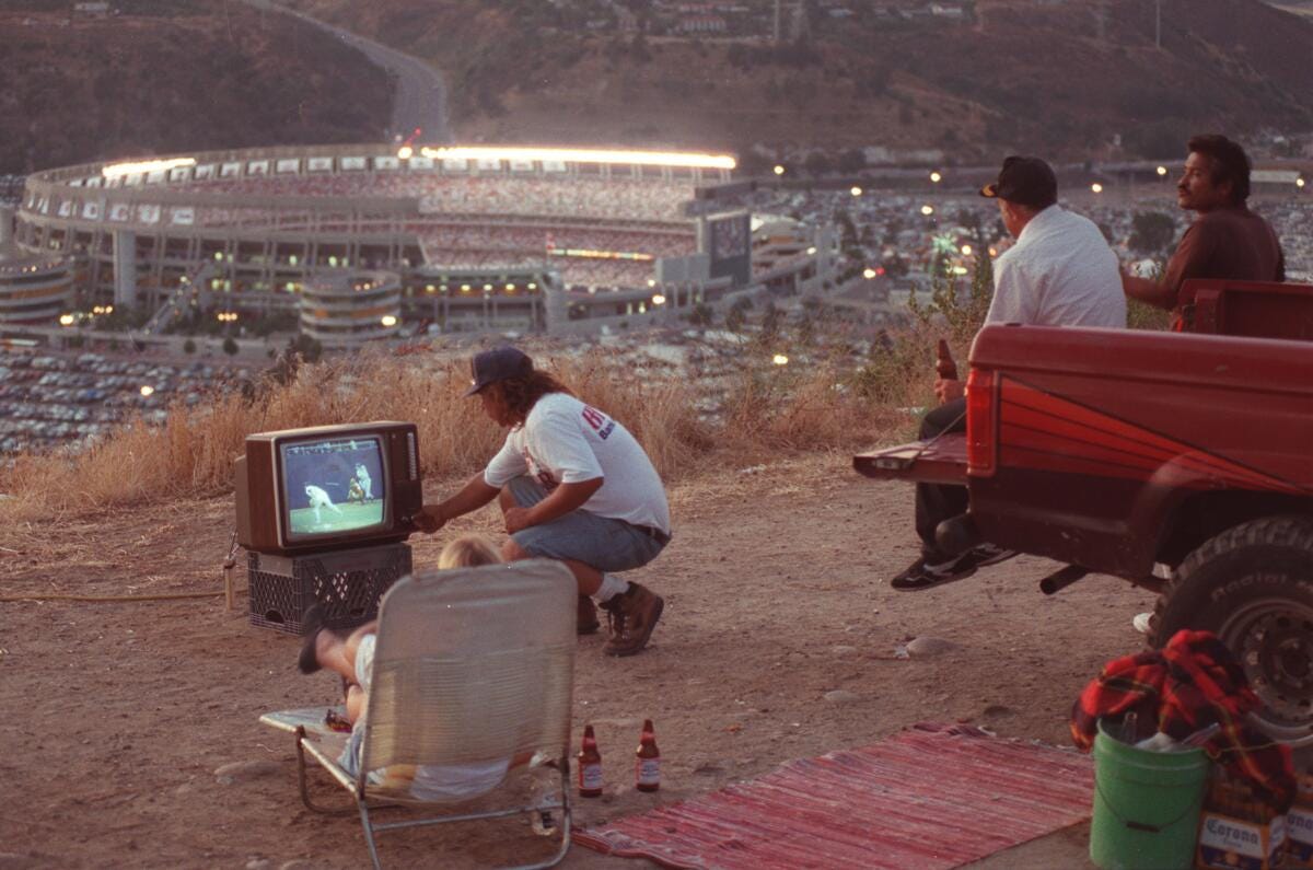 A man  adjusts a tv set as he and  friends watch the 1992  All-Star Game from a pickup above San Diego Jack Murphy Stadium 