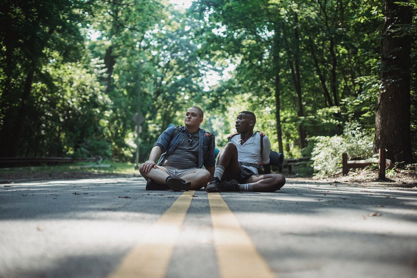 Two male hikers sitting in the middle of the road