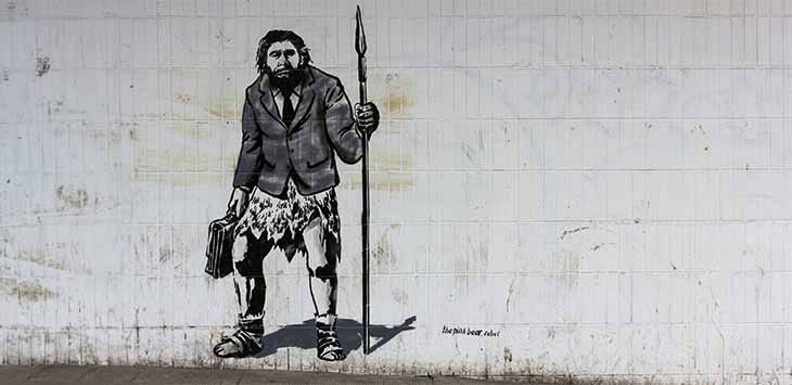 Photo of a mural of a caveman wearing a suit jacket and carrying a spear and a briefcase.