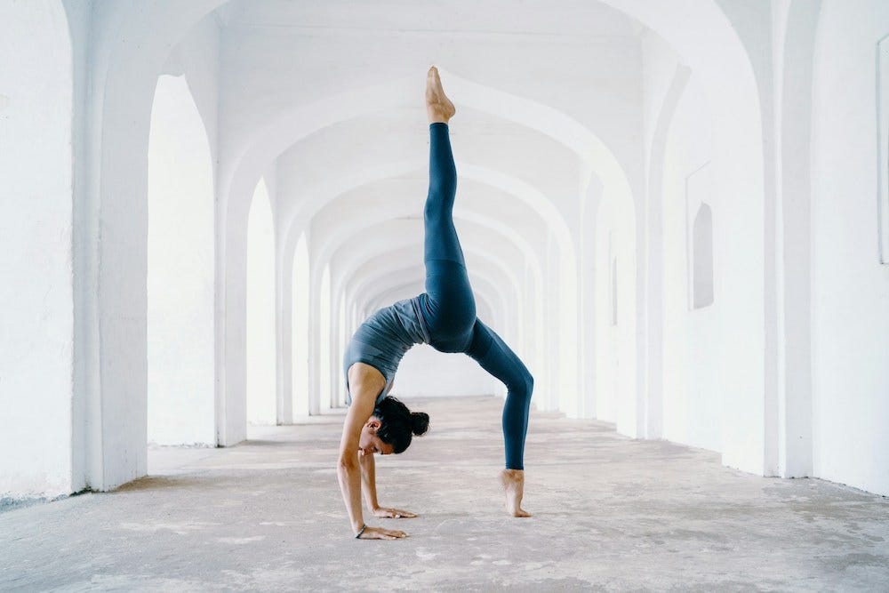 a woman performs a difficult yoga pose in a white hallway of a very old building