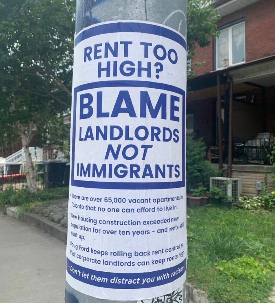 A sign says "rent too high? blame landlords not immigrants"