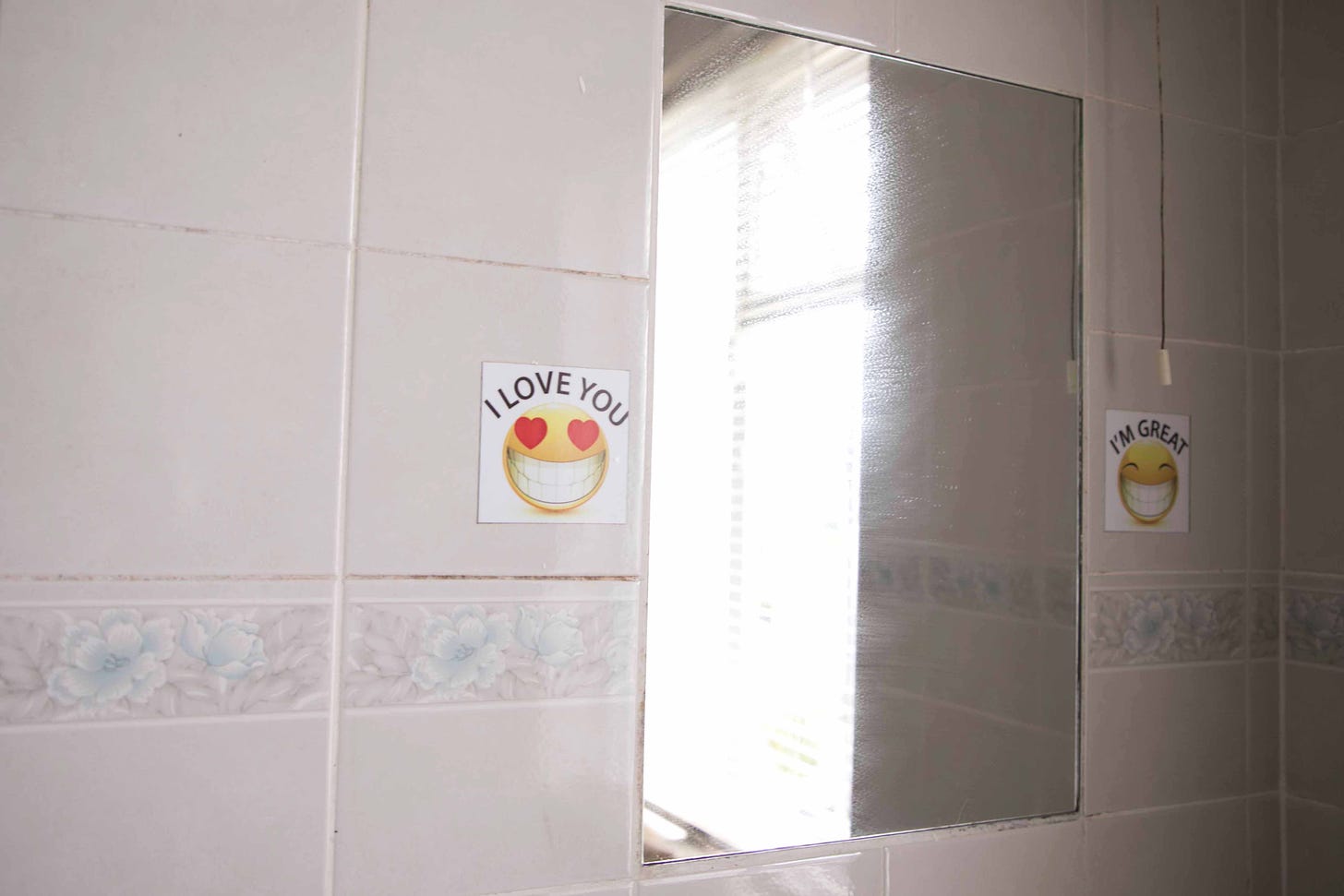 Emoji stickers that say "I love you" and "I'm great" are stuck on either side of a bathroom mirror in Ireland with the sun reflected in the mirror but no face. Photo credit: Nancy Forde. All rights reserved. nancyforde.com