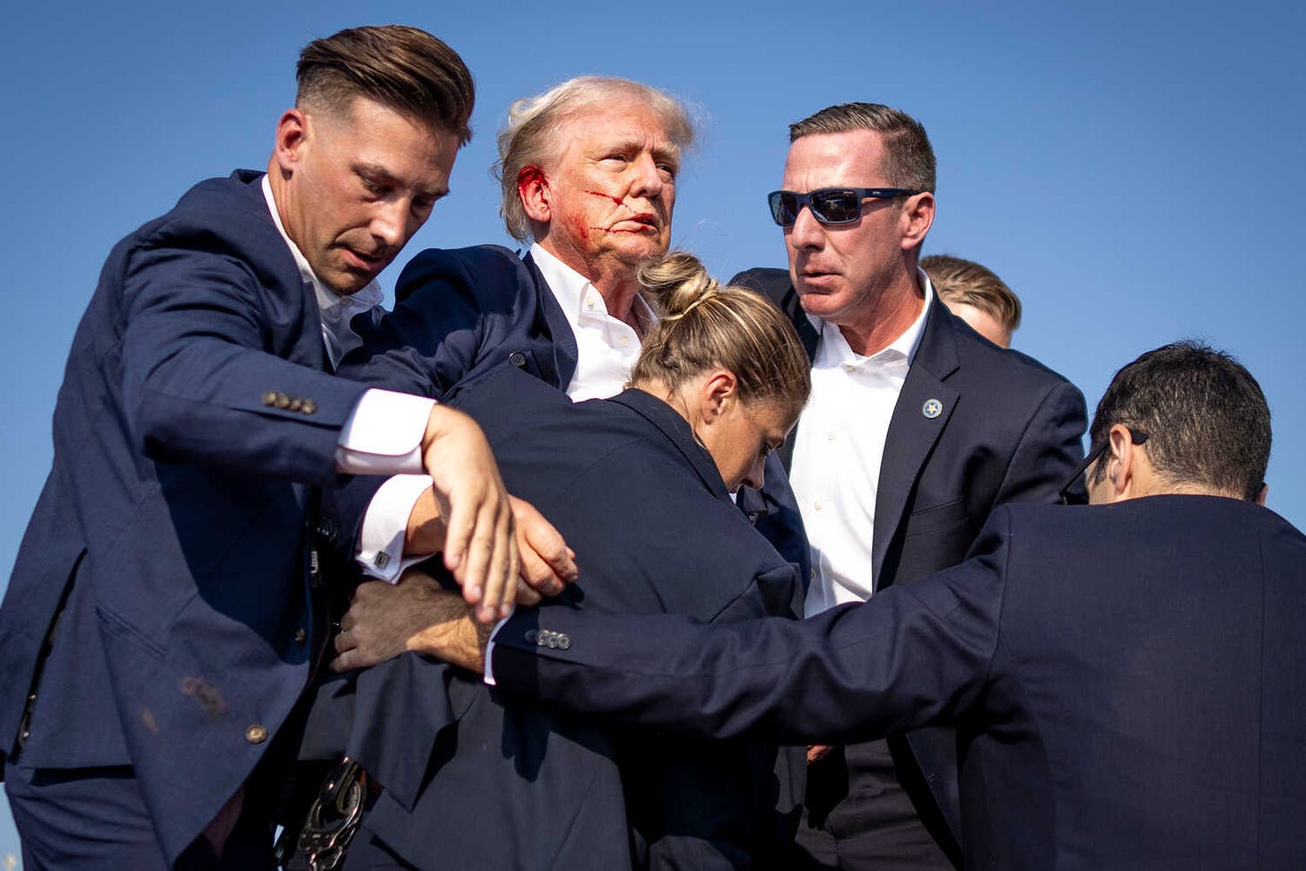 Donald Trump, bleeding from an ear and surrounded by Secret Service agents.