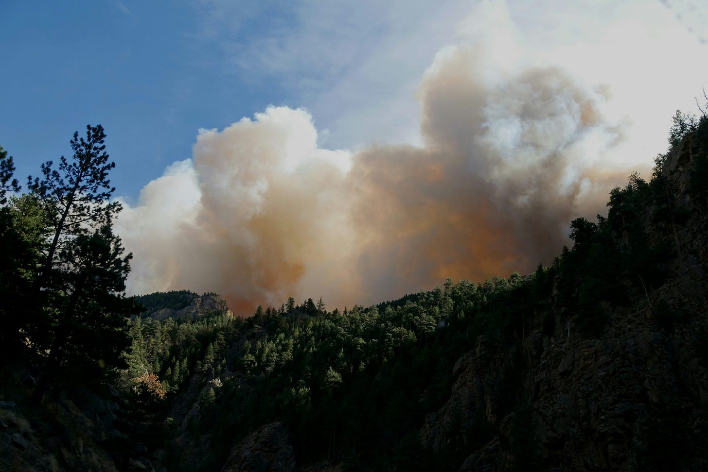 Orange smoke rising from behind a forested hill