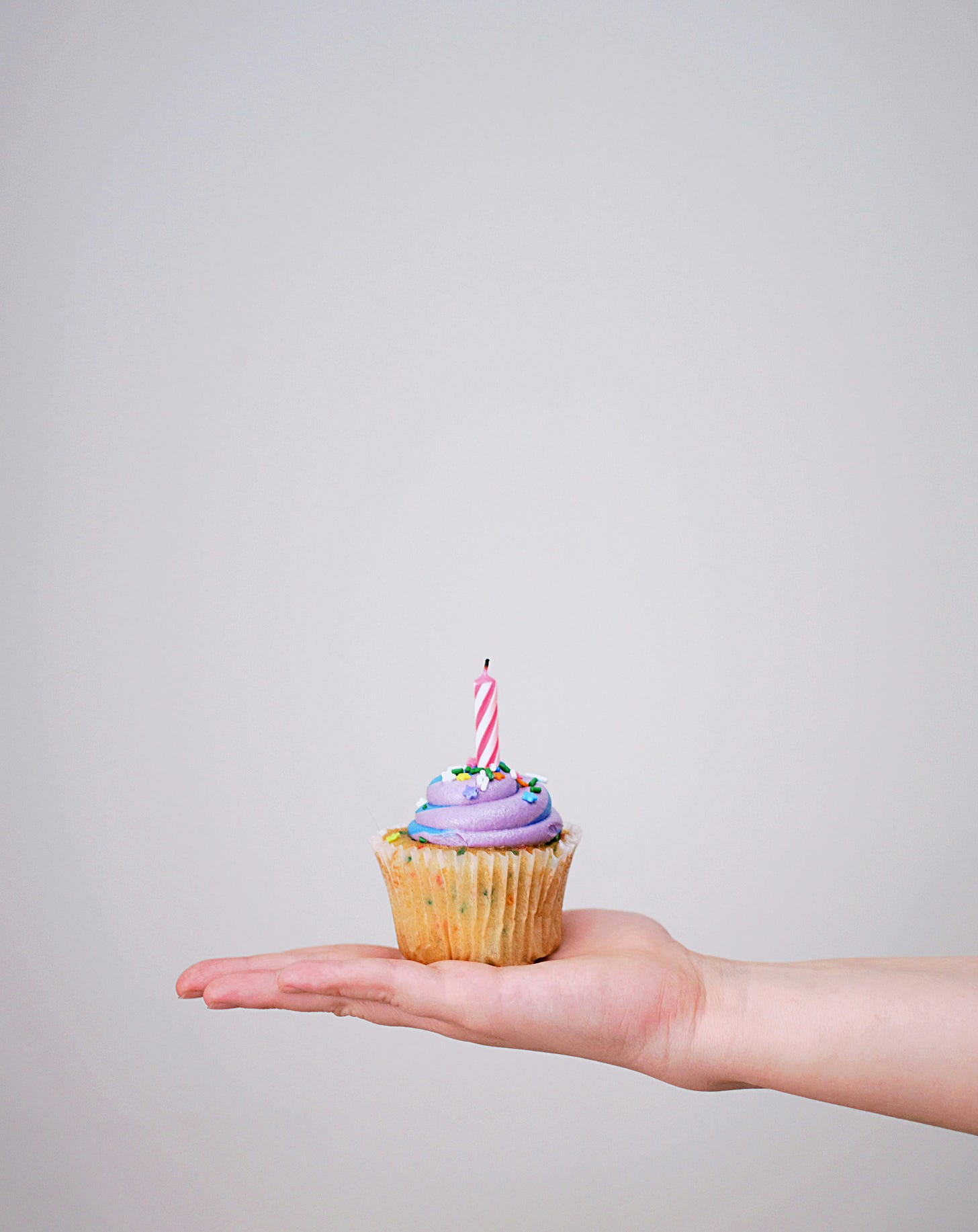 Una mano con il palmo all'insù tiene una piccola cupcake con crema viola e una candelina rossa e bianca