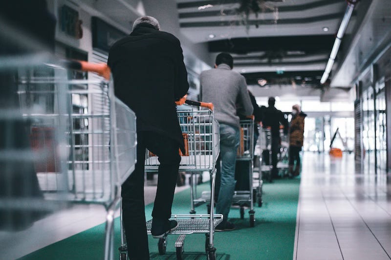 A group of shoppers queueing outside of supermarket with empty trolleys