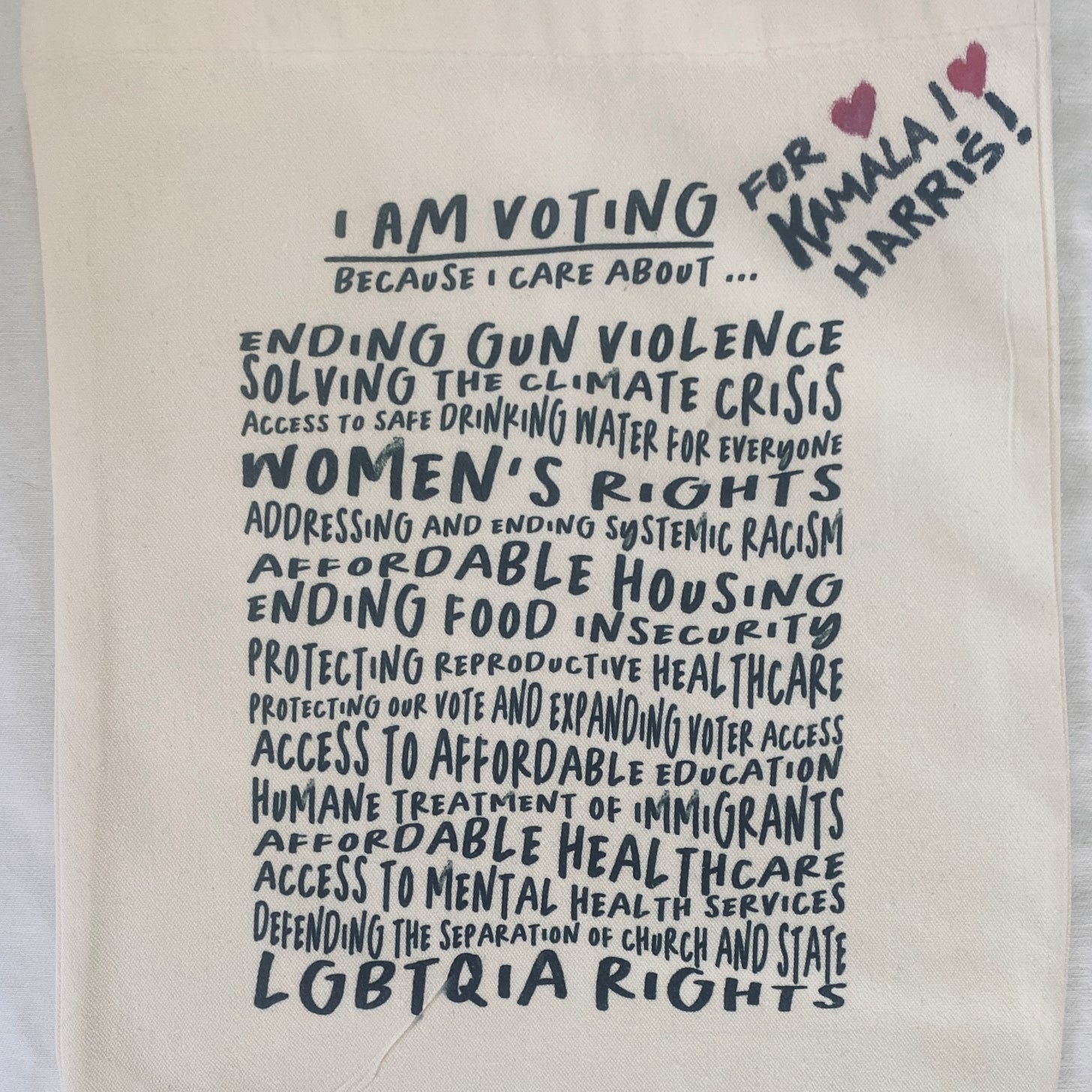 A canvas bag with handwritten font saying I am voting [for Kamala Harris] because I care about... Ending gun violence. Solving the climate crisis. Access to safe drinking water for everyone. Women’s rights. Address and ending systemic racism. Affordable housing. Ending food insecurity. Protecting reproductive healthcare. Protecting our vote and expanding voter access.  Access to affordable education. Human treatment of immigrants. Affordable healthcare. Access to mental health services. Defending the separation of church and state. LGBTQIA rights. 