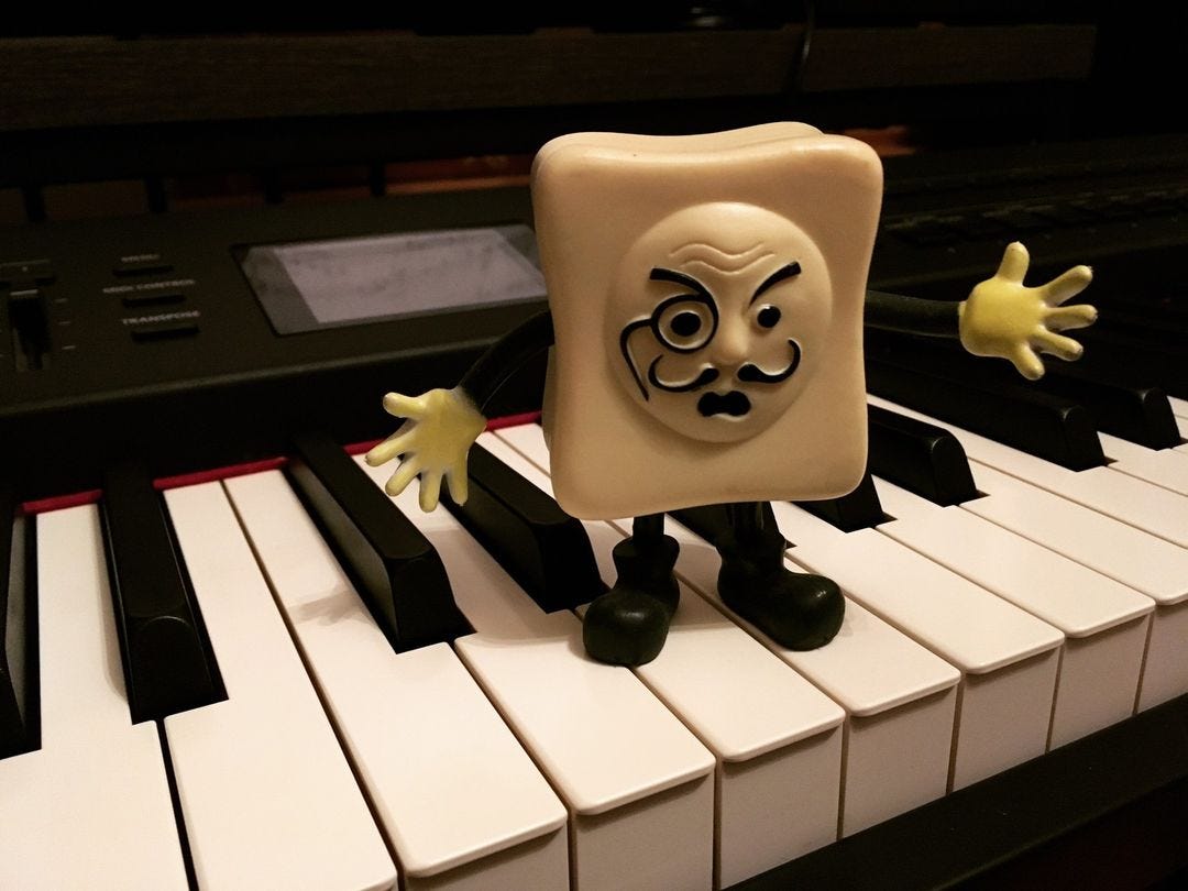 A Monsieur Tofu action figure staring angrily into the camera while standing atop a piano keyboard.