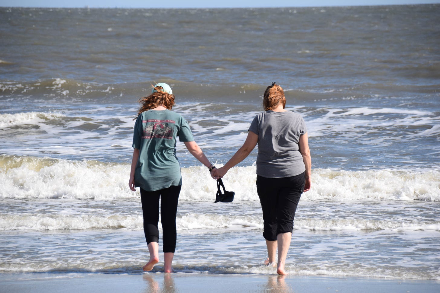 The author and her daughter walking hand in hand into ocean waves.