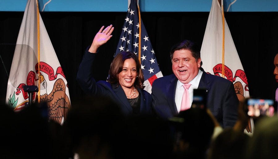 Vice President Kamala Harris and Illinois Gov. J.B. Pritzker, both clad in dark suits, smile as they stand in front of American and state flags during a rally in Chicago.