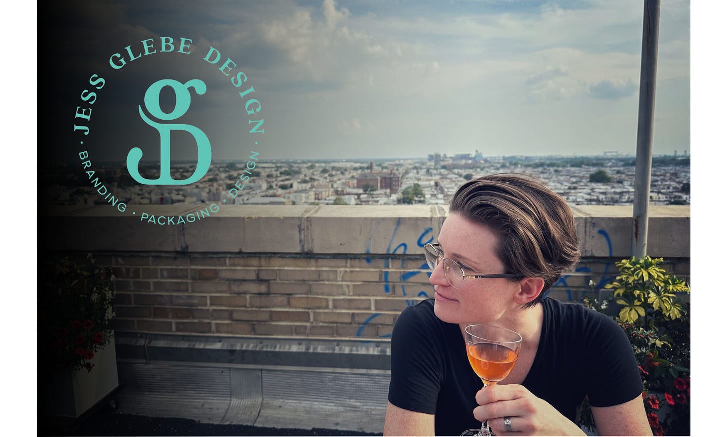 A woman drinks a glass of wine on a rooftop with the cityscape spanning out under a cloudy blue sky behind her.