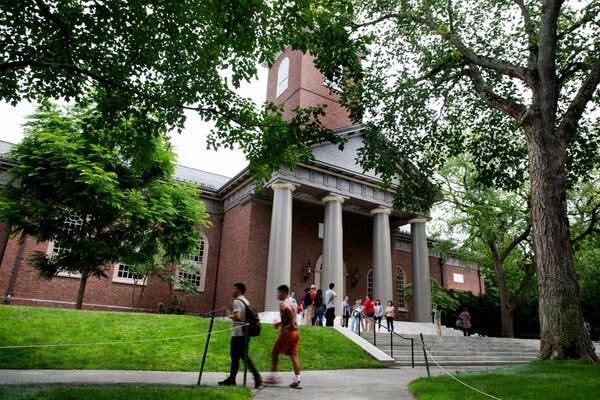 Students walking in front of a red brick building with a columned entrance on Harvard’s campus.