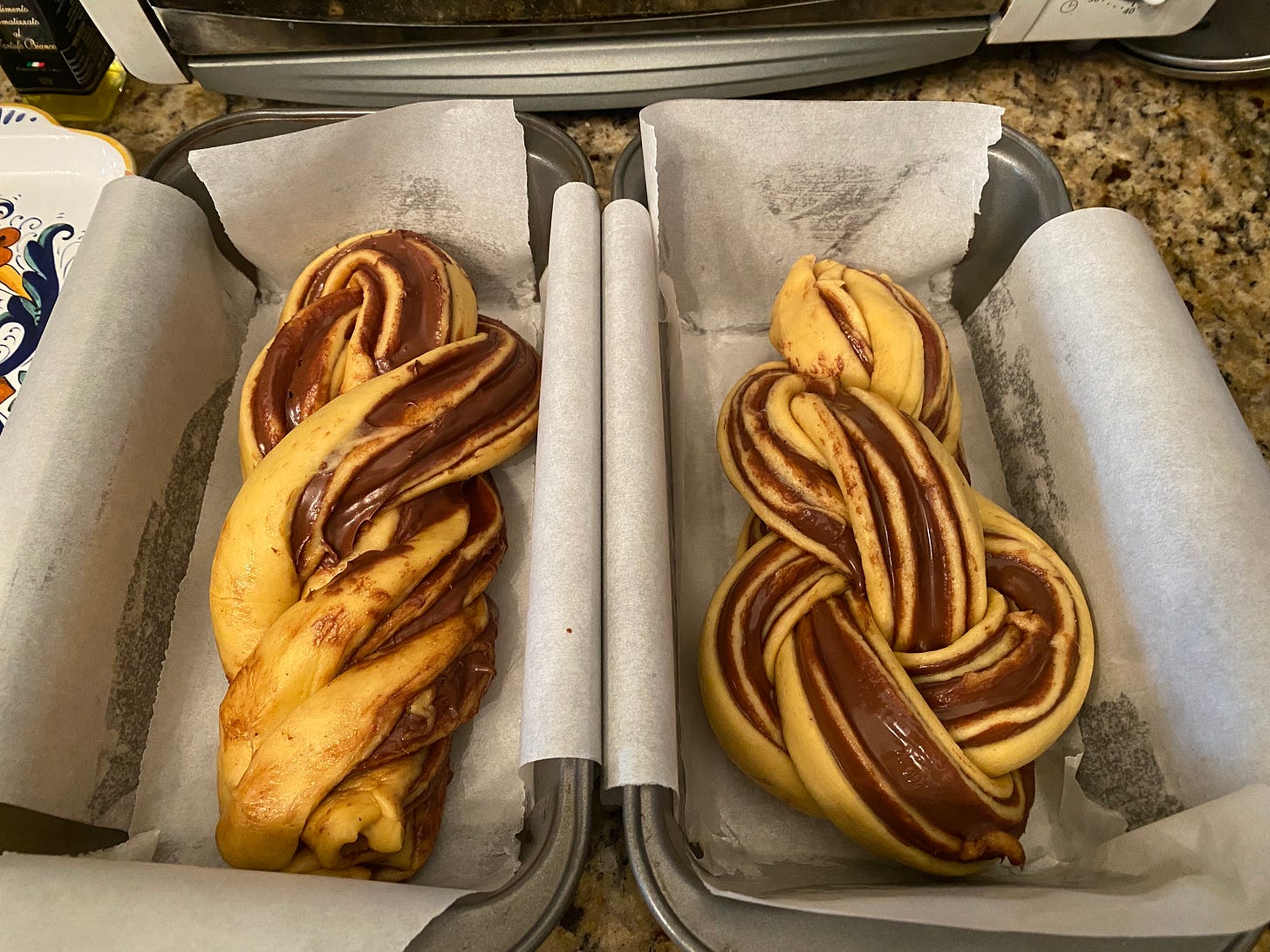 Two loaf pans lined with parchment, each with a stripey braid of unbaked dough inside. The one on the right is a little less messy-looking.