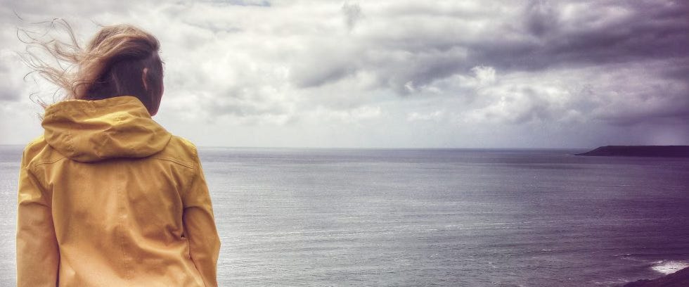 A woman in a yellow raincoat looking out over the sea.