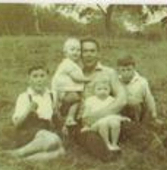 Old black and white photo of father with his three sons and a daughter, all seated on grass, with trees in the background