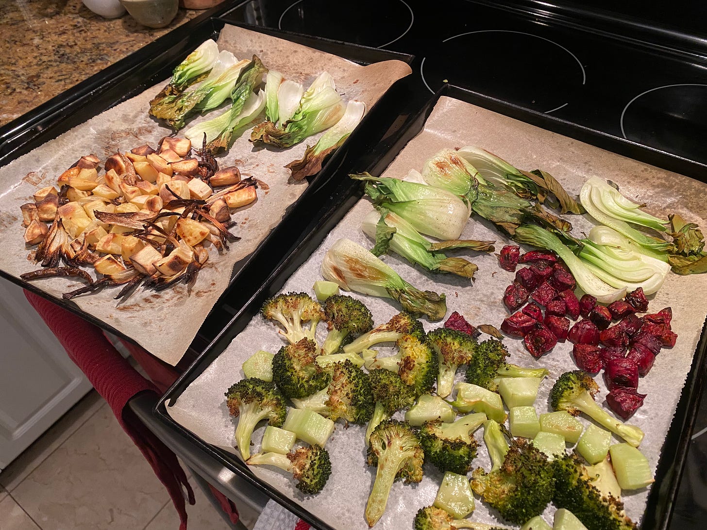 The roasted vegetables for the bibimbap, arranged in sections on two sheet pans. The left has white sweet potato and slices of onion at the front and bok choy at the back. The right has broccoli at the front, beets in the centre, and more bok choy at the back.