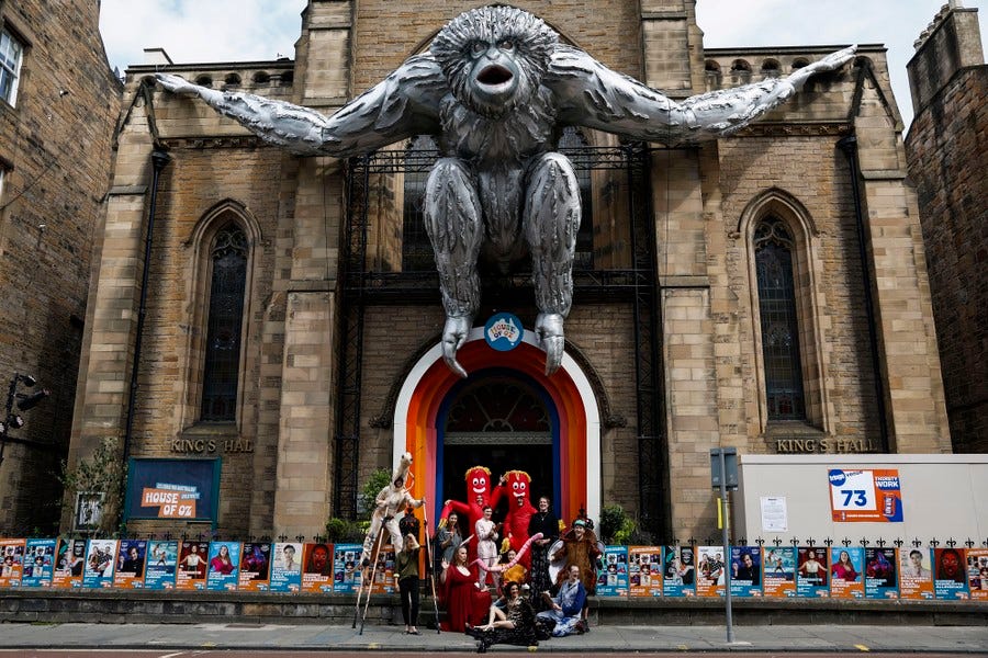A group of performers stands in front of a venue, beneath a large inflatable gibbon.