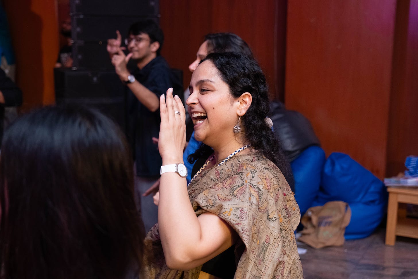 Tania is an Indian woman with long black hair pulled back. She is dressed in a beige saree with kantha embroidery and is signing with a few other participants at the Change the Script event. A blue and a black bean bag can be seen in the background.