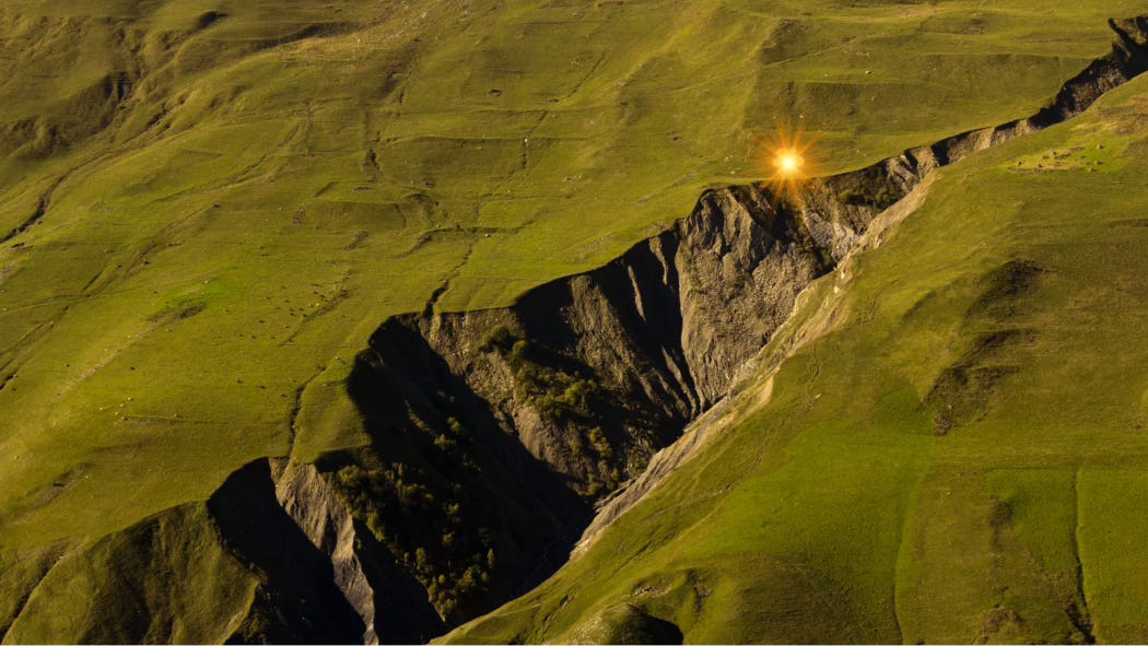 A jagged ravine cracks through the lush green landscape. On one of its edges, an eerie golden light glows.