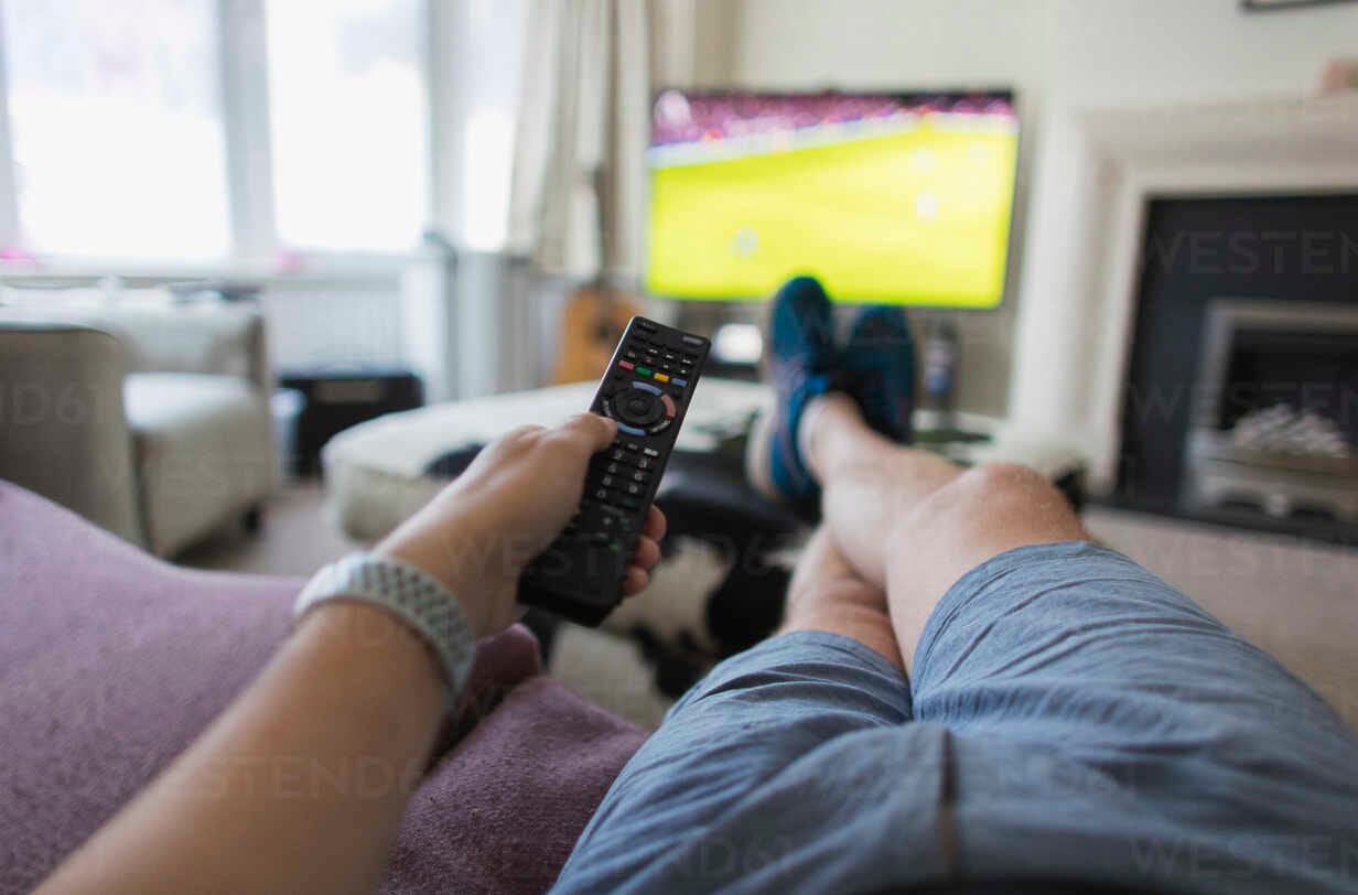 POV man with remote control watching soccer match on living room sofa stock  photo