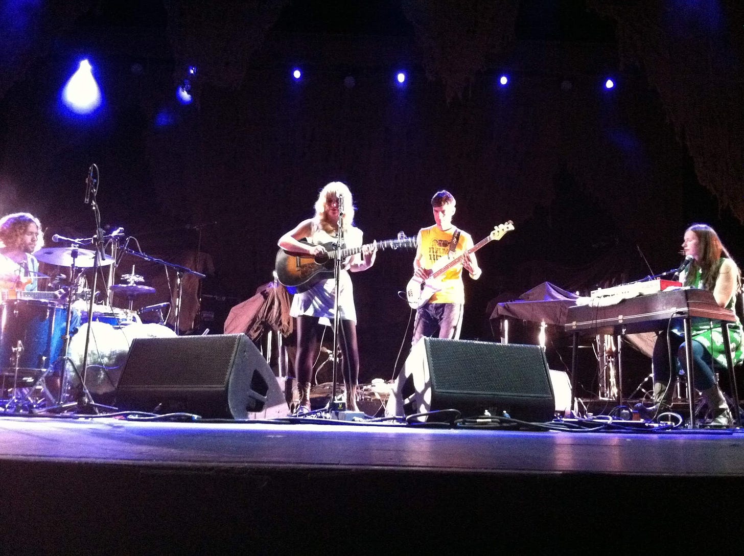 Picture of Anais Mitchell playing at radio city. She is holing a guitar in the middle with the drummer to her left, bassist close on her right and electric piano player further right. 