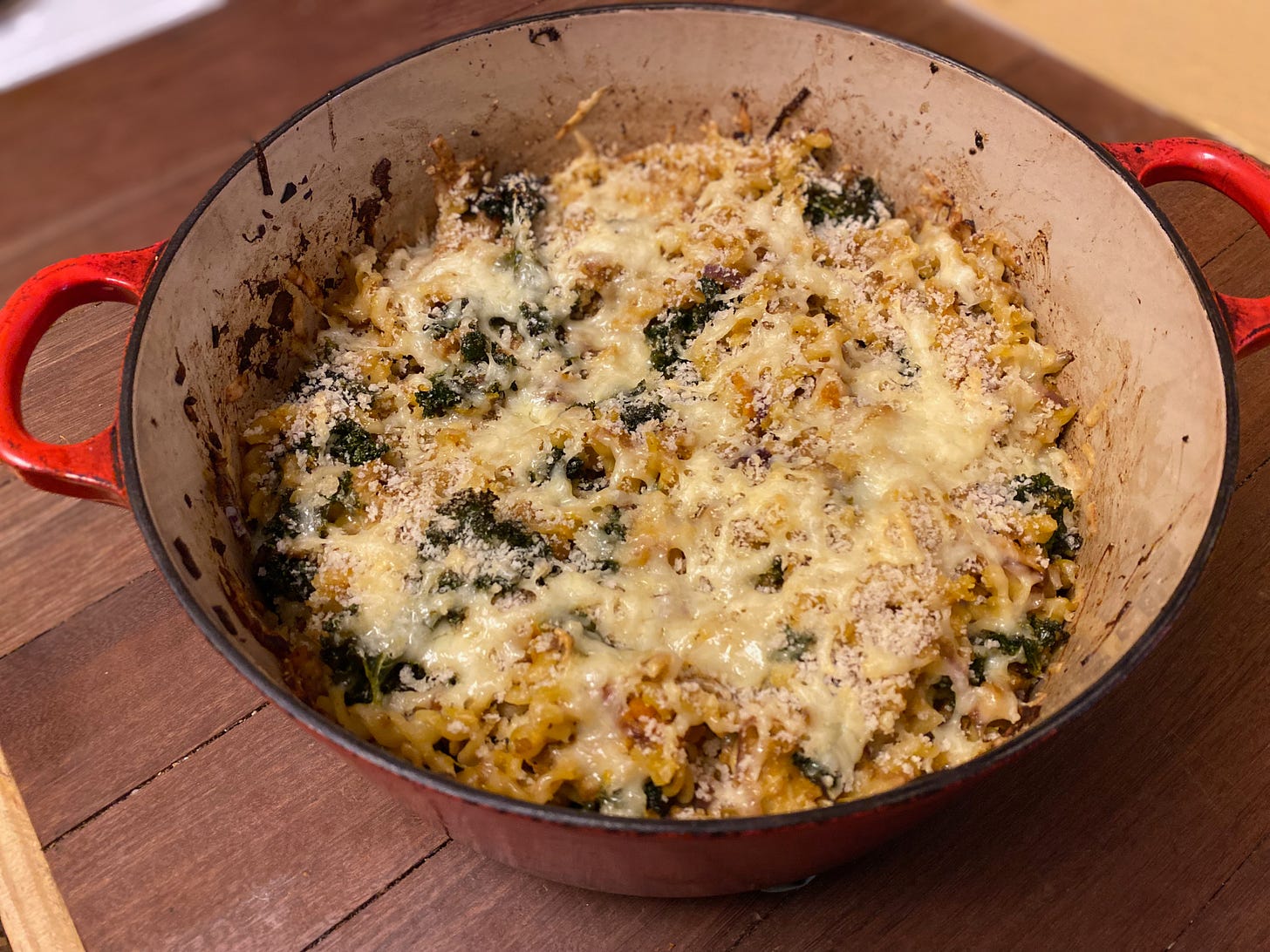 A large dish of baked pasta, covered with melty cheese, sits on a wooden counter.