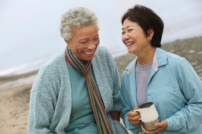 Two elder women enjoying their time together encouraging each other while walking on the beach