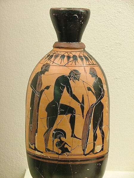 Photograph of a black figure vase with a nude warrior putting greaves on