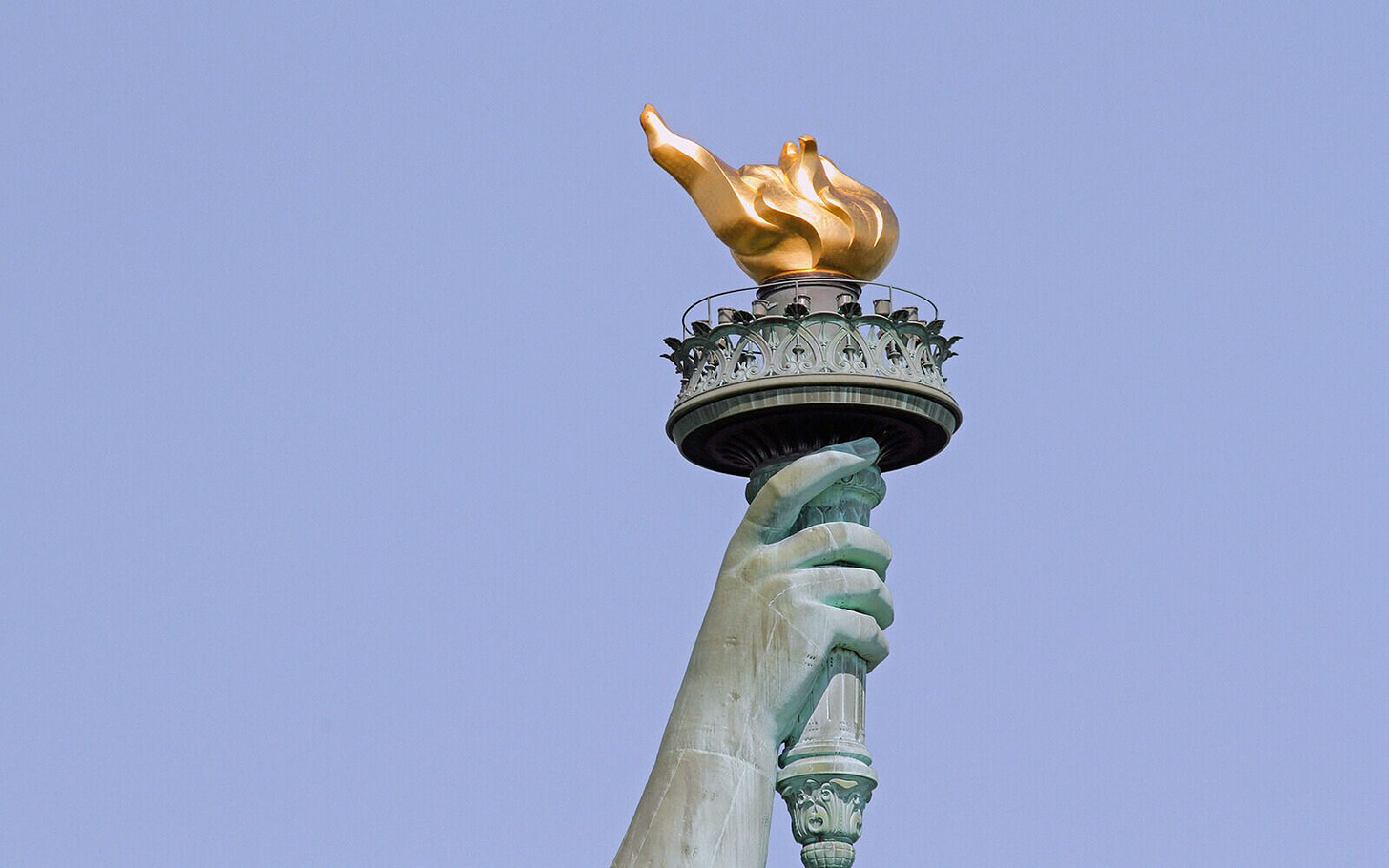 a closeup of the statue of liberty's hand clutching the torch against a blue sky