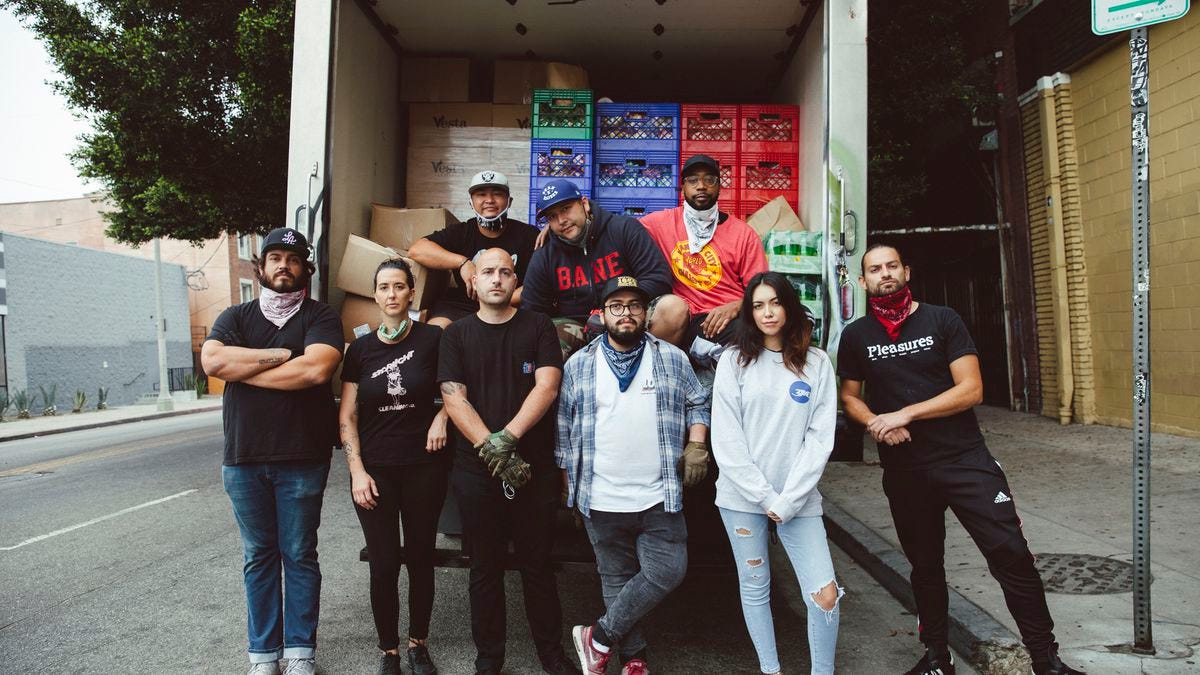 Nine people standing in front of an open truck containing crates of donated food.
