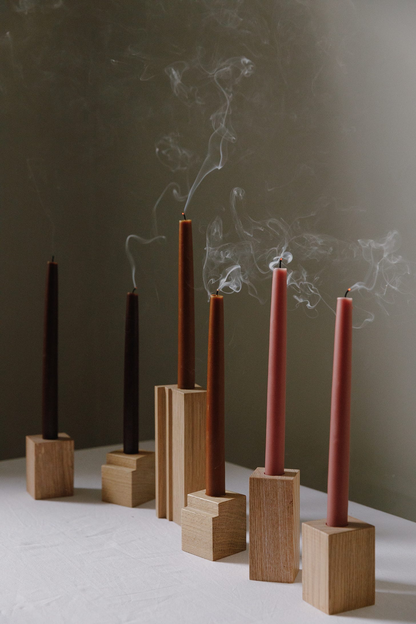 six dinner candles in a row on a tabletop that are smoking as they have just been blown out