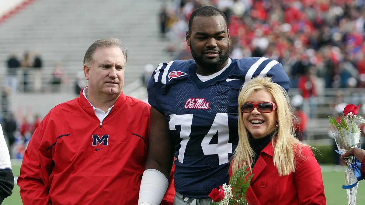 Football player Michael Oher standing with Sean and Leigh Ann Touhy on the field at a college football game