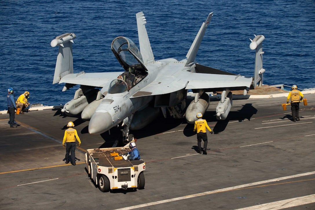 A military aircraft is transported on a Navy ship's flight deck.