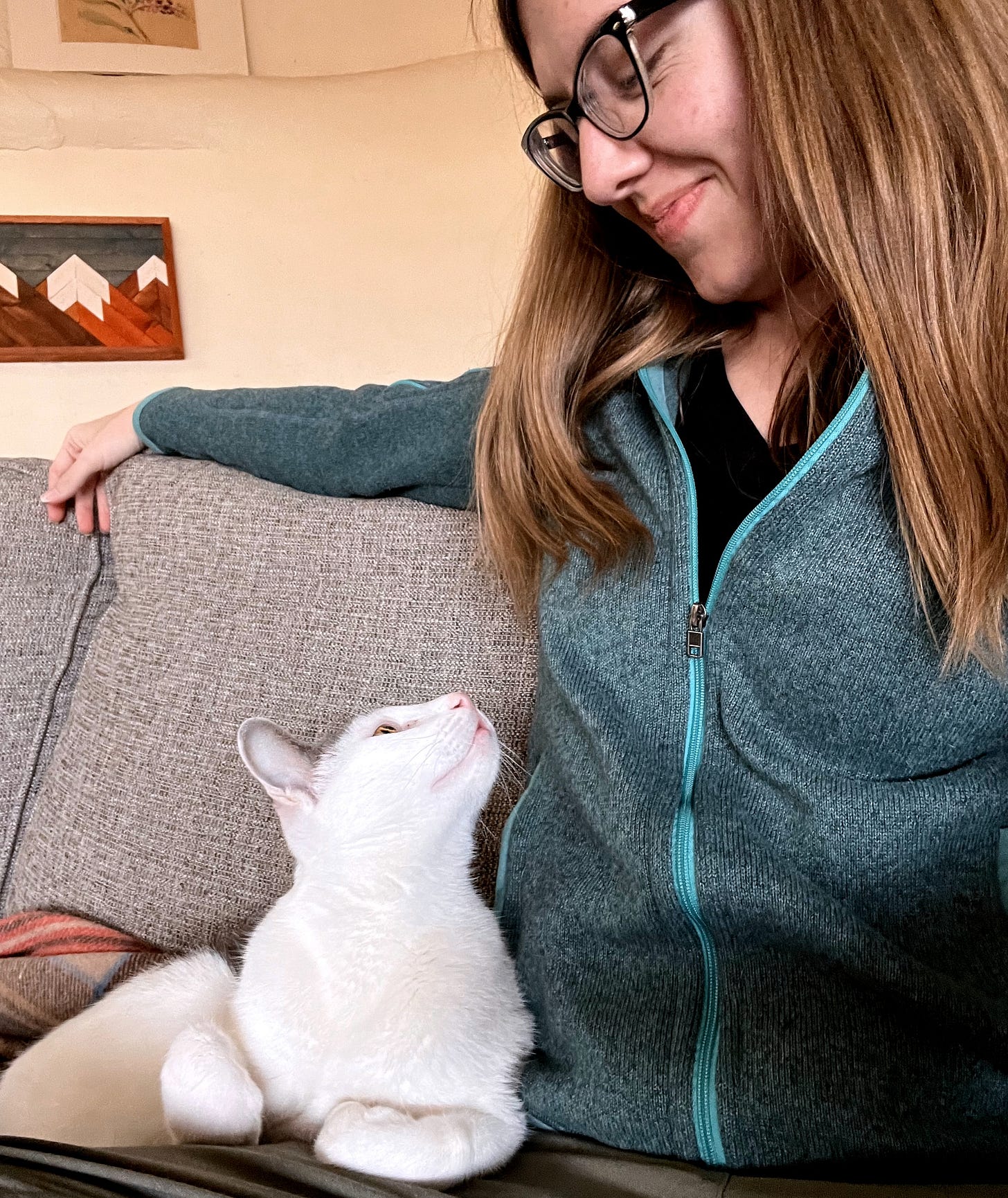 A photo of a woman and cat sitting together on a couch, gazing into each other's eyes.