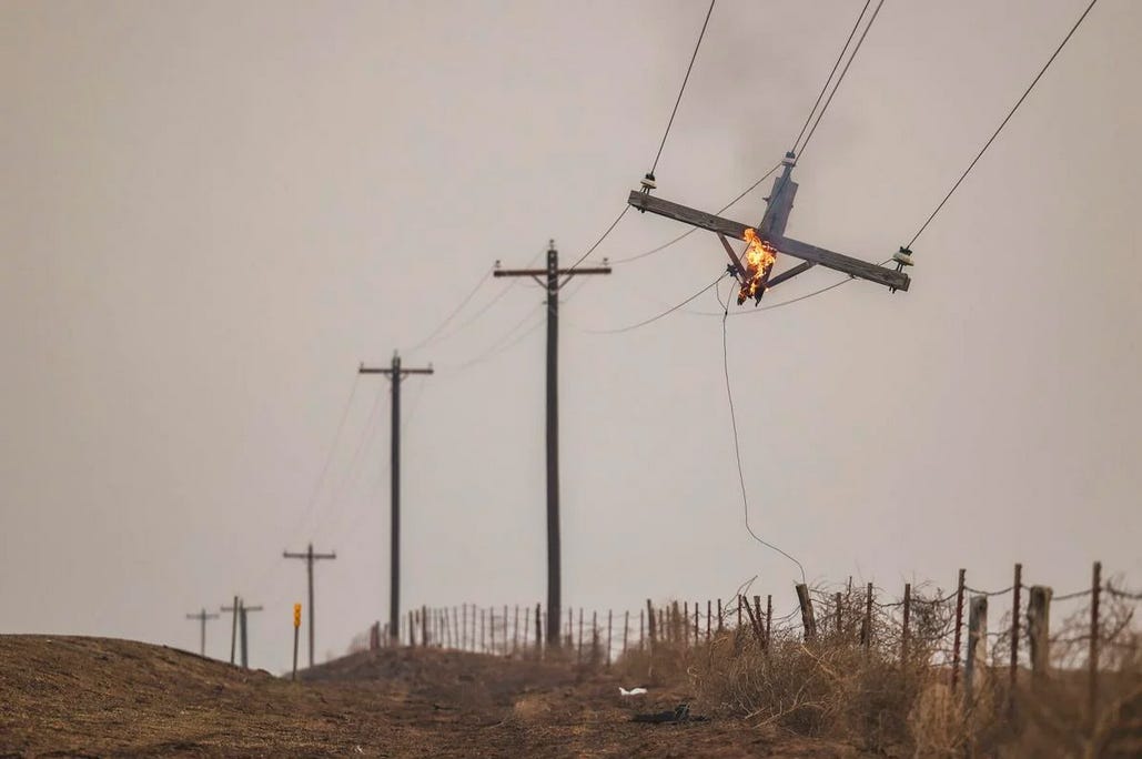 The top of a utility line pole hangs, flaming in the air, the rest of the pole gone.
