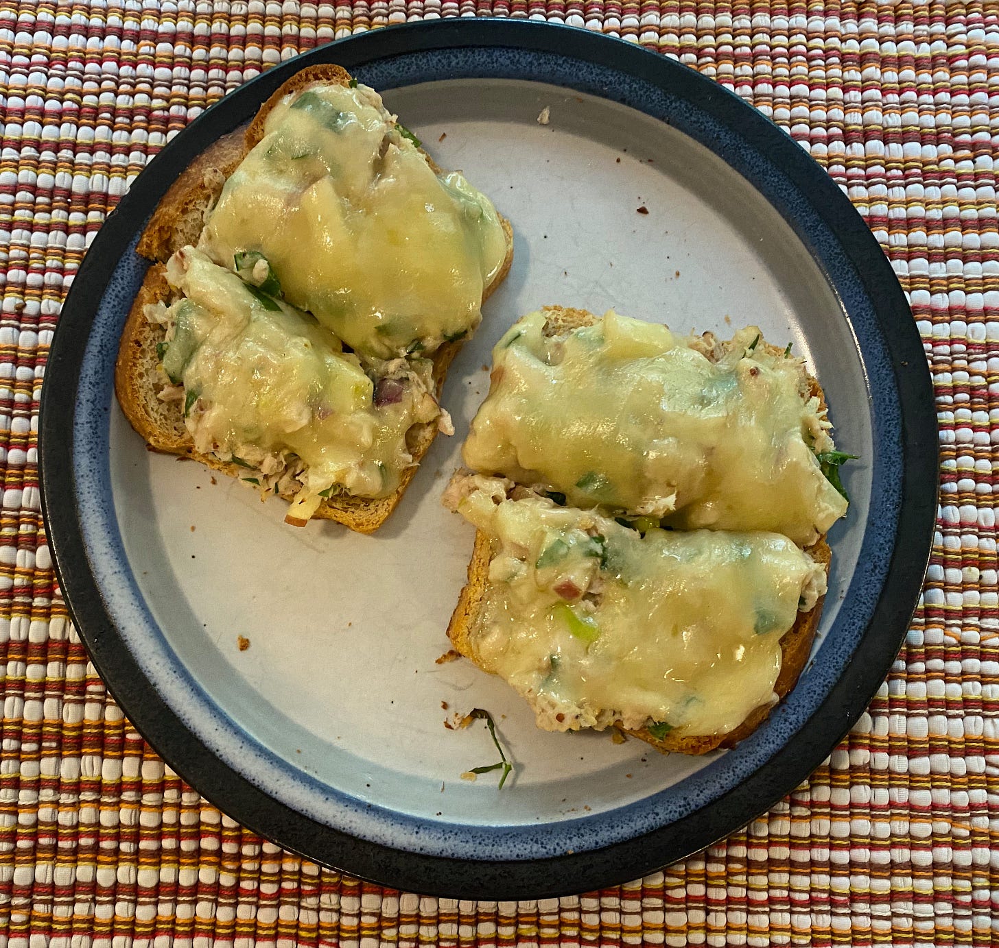 A small ceramic plate with two open-faced tuna melts cut in half.