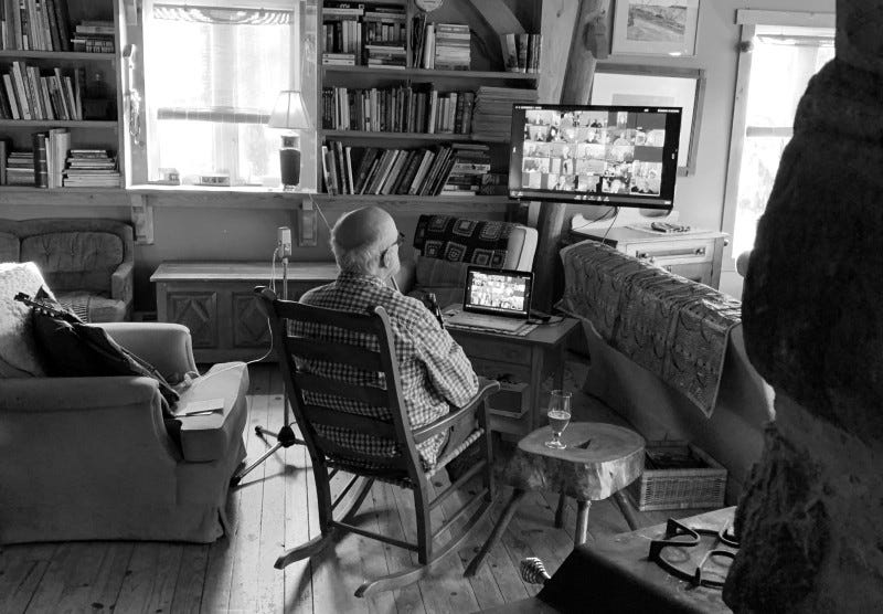 Musician watching and participating in an online fiddle teaching session, in a rocking chair in front of a tv screen.