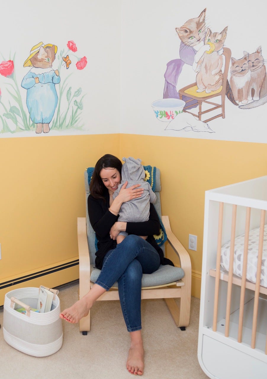 woman holding baby with beatrix potter characters painted in background woman holding baby with beatrix potter characters painted in background