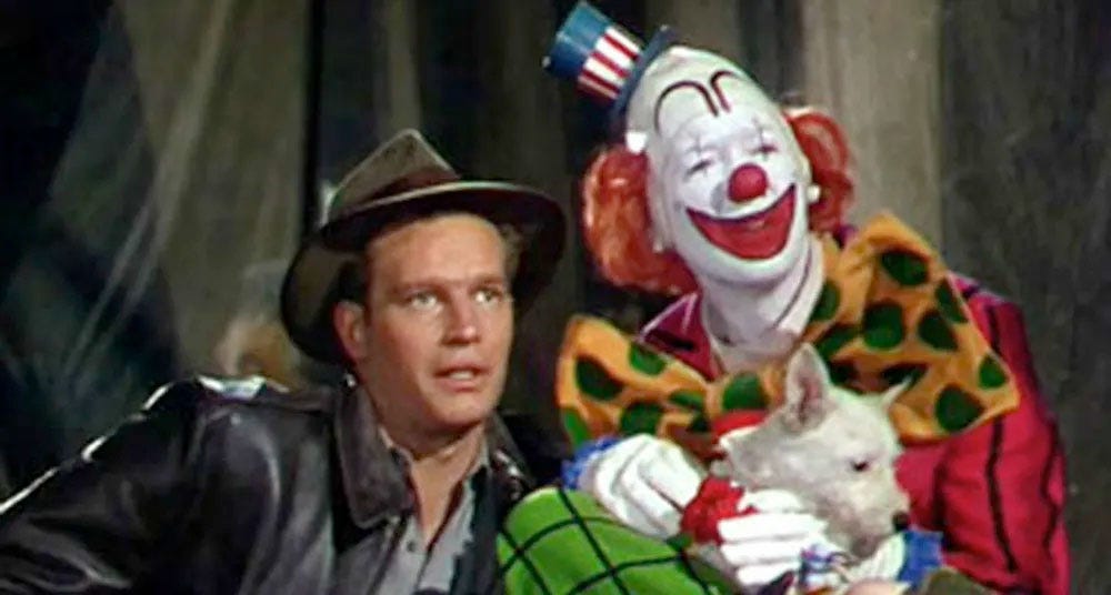 Charlton Heston and James Stewart in Cecil B. DeMille's 1952 Hollywood epic The Greatest Show on Earth. Heston wears a natty fedora and a leather flying jacket. Stewart wears full clown make-up and costume and holds a small white dog