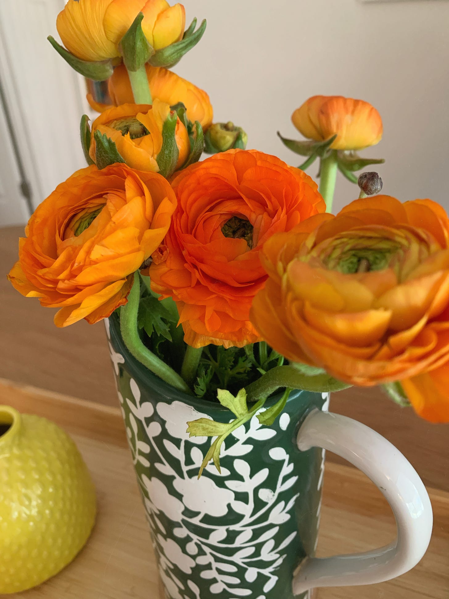 Orange ranunculus in a ceramic pitcher, placed on a dining room table.