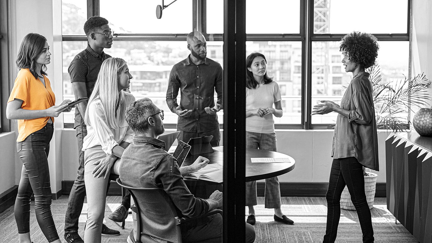 A group of people listen to a woman explain an idea intently.