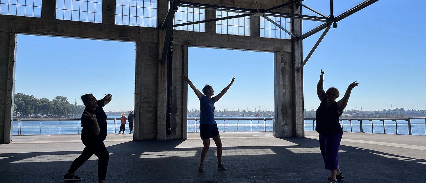 Three people with arms reaching in silhouette with the Bay in the background, visible through cement square cutouts. Three people with arms reaching in silhouette with the Bay in the background, visible through cement square cutouts.
