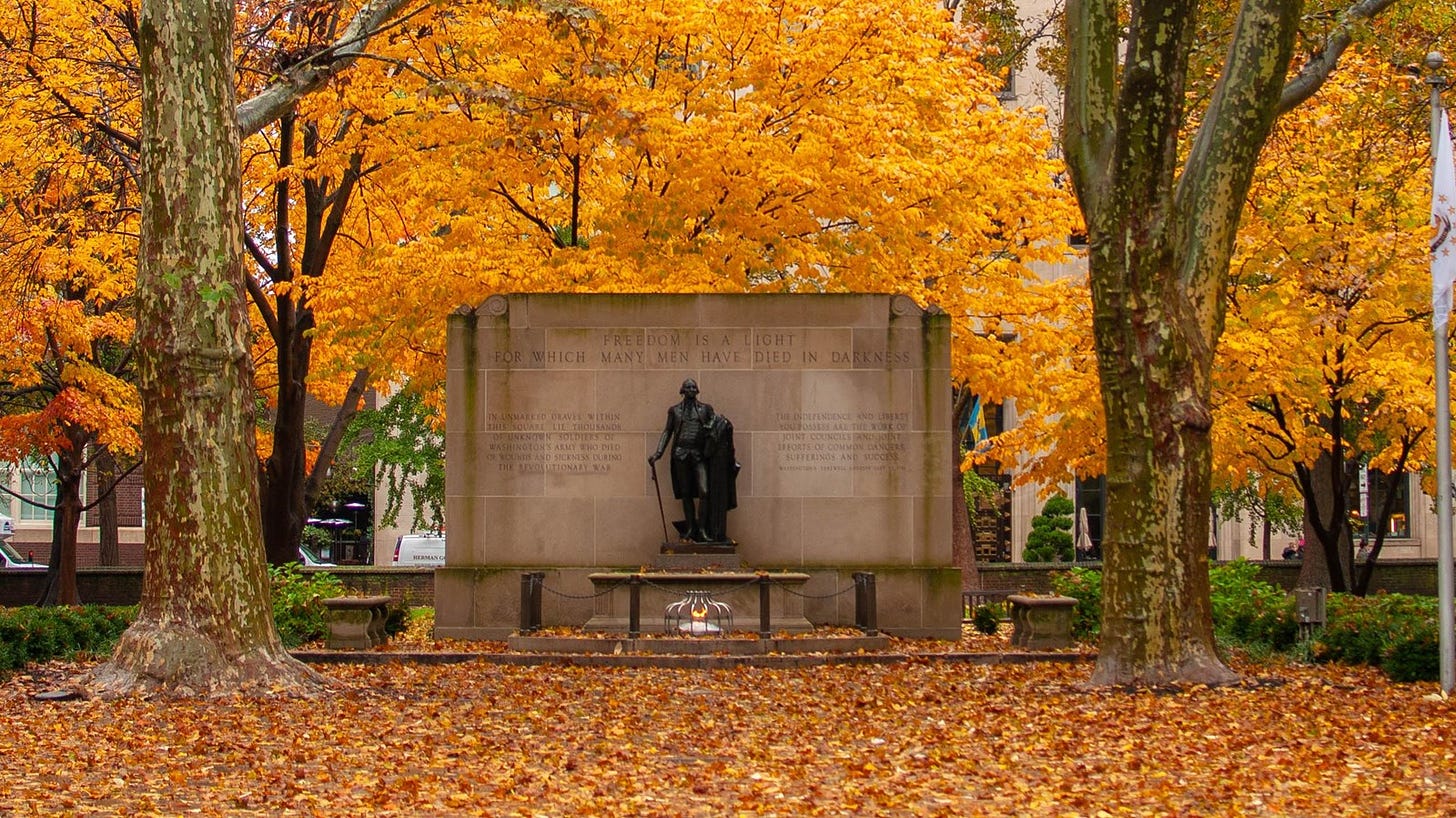 A color photo showing a statue in front of monument surrounded by yellow and orange fall foliage