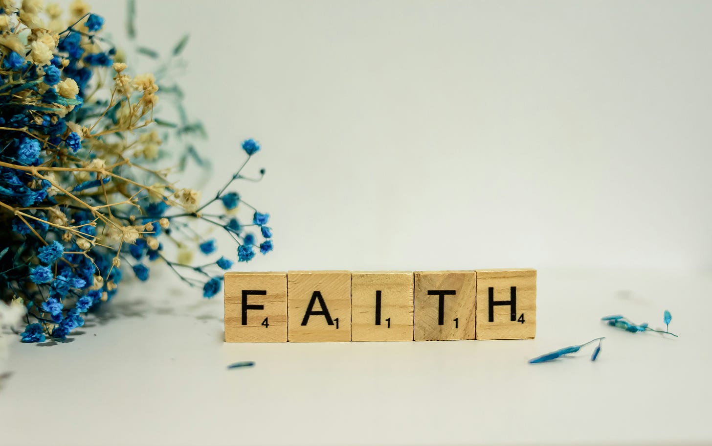 The word faith spelled in Scrabble letters with a white background and blue and cream colored flowers 