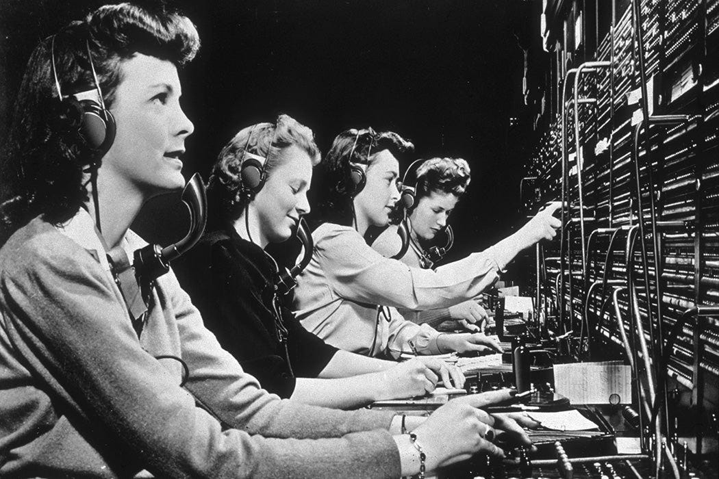 Four operators connect calls while working at a switchboard.