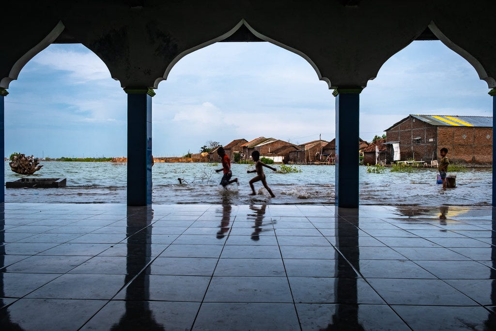 Children are playing in the flooded yard in front of a mosque due to rising sea levels. Sayung subdistrict, Demak, Central Java, Indonesia.