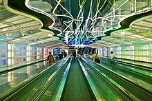 Picture of Michael Hayden's Sky's the Limit at O'Hare International Airport. It is a moving walkway with neon lights of varied colors overhead.