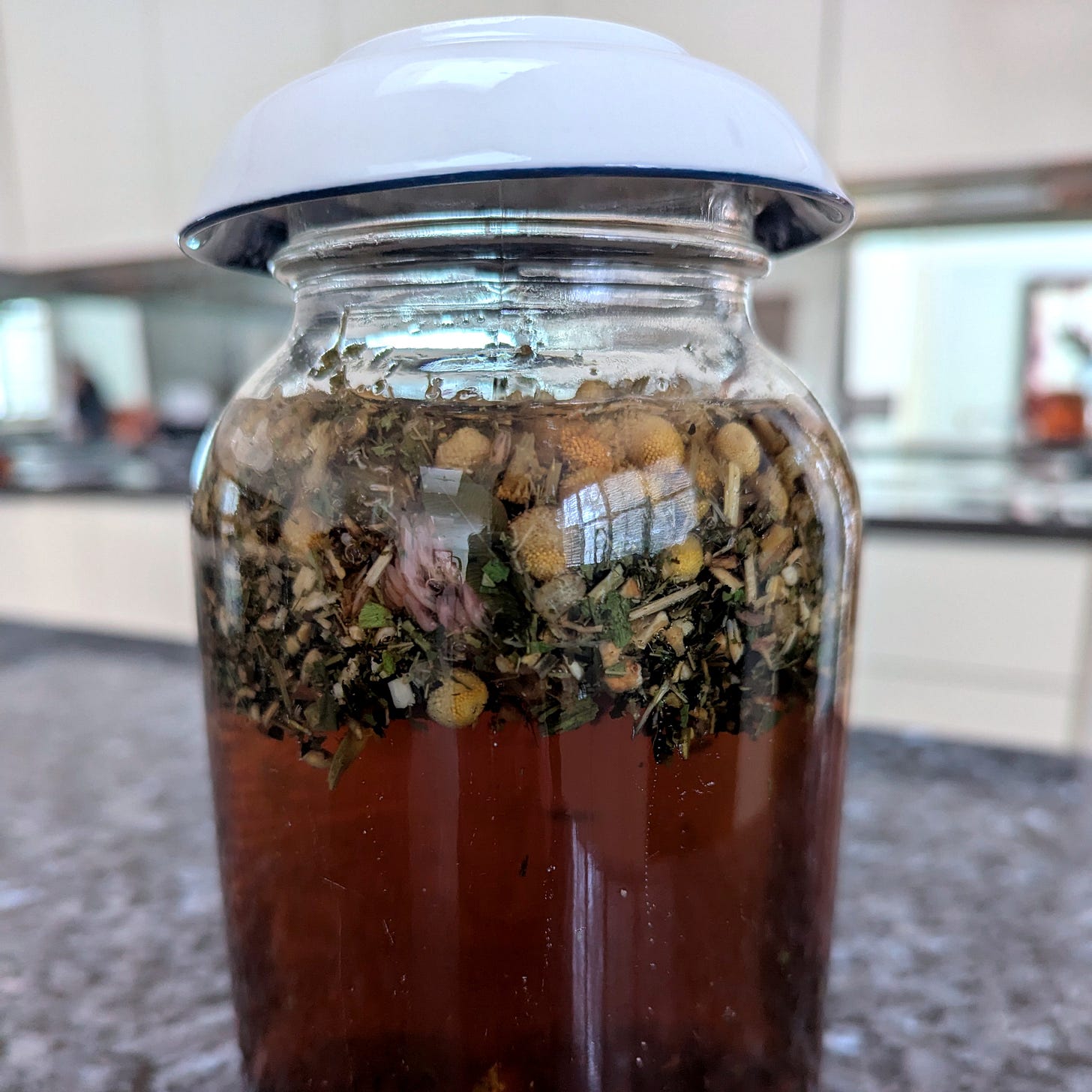 A photo of a mason jar of loose leaf herbal tea on a grey marble counter, with mirrors in the back. A photo of a mason jar of loose leaf herbal tea on a grey marble counter, with mirrors in the back.